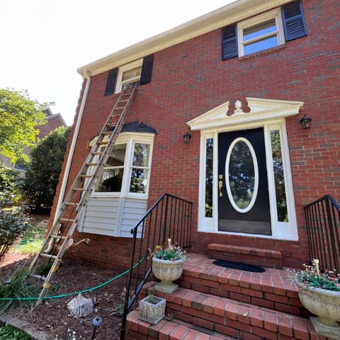 Brick house with its white trim and door surround being repainted, ladder against the wall