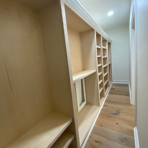 Built-in shelving wrapped around a corner window nook, ready for paint