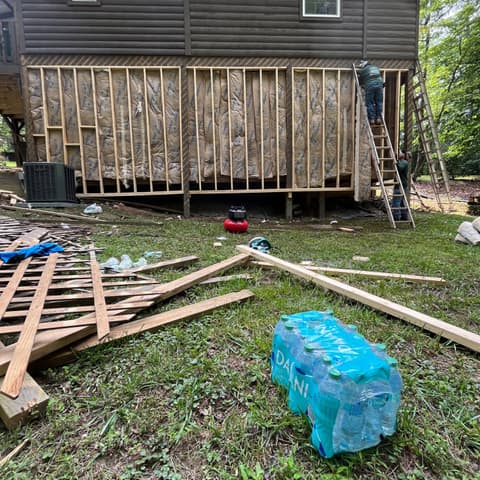 Log cabin deck being reframed, the old boards stacked on the lawn below