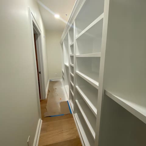 Hallway lined with finished white built-in shelving over a wood floor