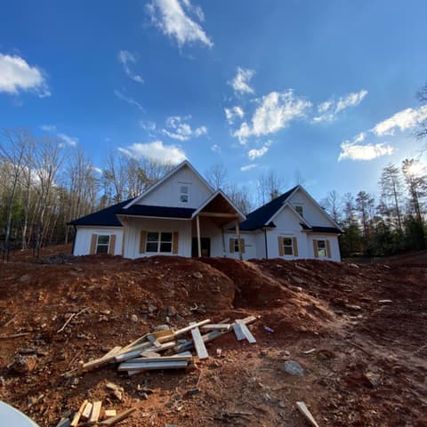 New house with a covered porch, siding on, on a cleared red-clay lot