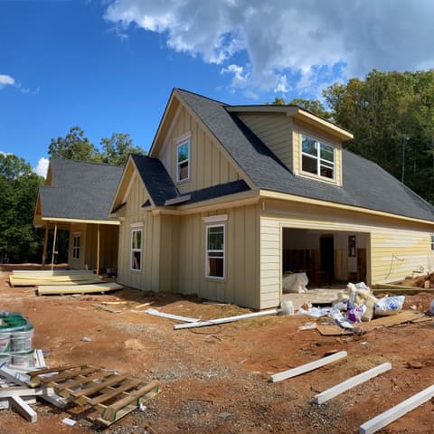 New house with a dormer, siding on, pallets of materials out front